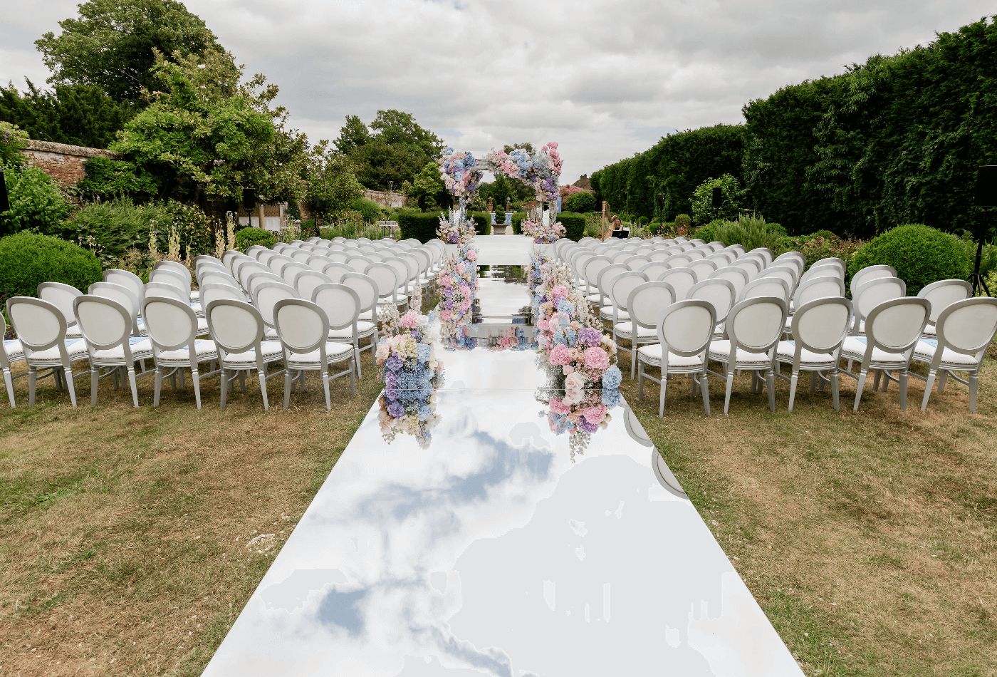 Outdoor wedding, ceremony set up on grass with white chairs and blue and pink floral arrangements.jpg