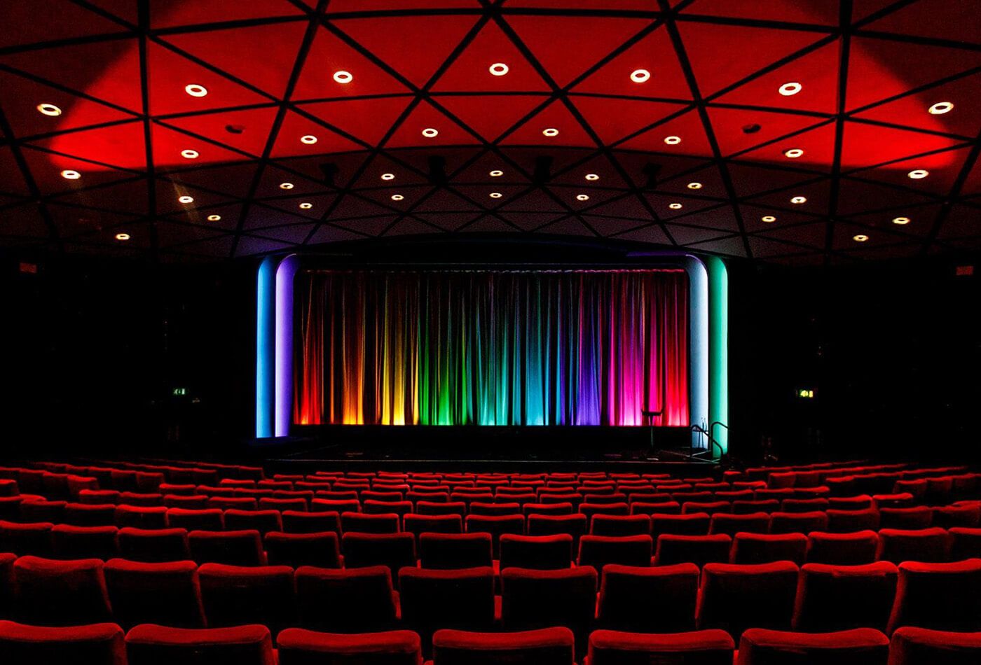 Interior shot of red velvet seats and stage lit with all colours of the rainbow