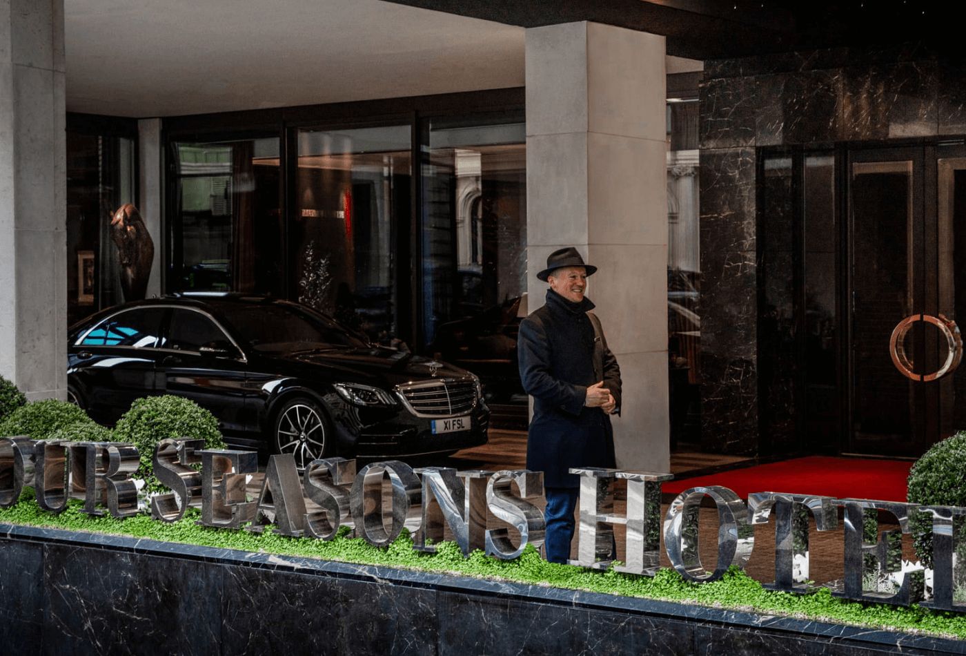 Man standing outside hotel in smart coat and hat.jpg