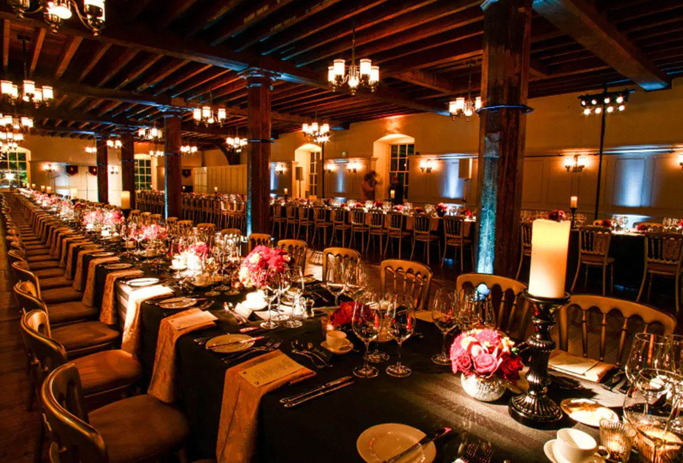Dark, long table wedding set up with golden chairs and wooden beamed ceiling