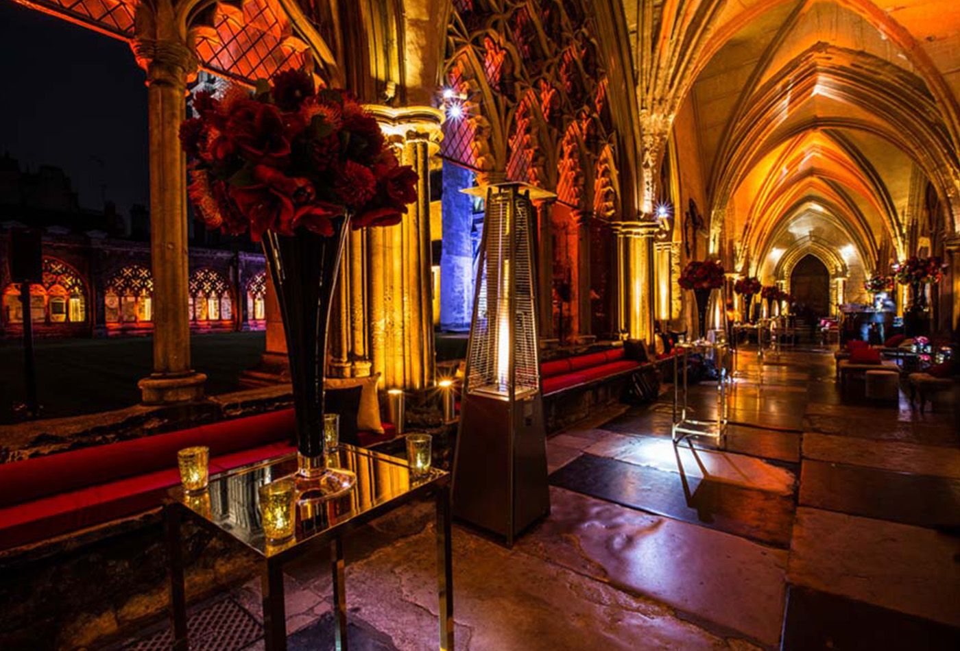 The main cloister at night, lit up with candles and decorated with red floral arrangements 