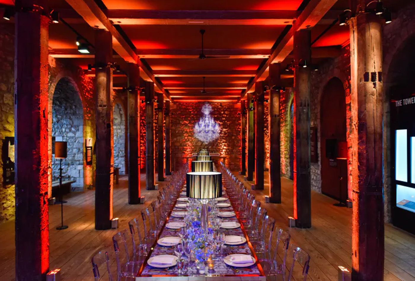 Grand dining space with brick walls lit up in red and long dining tables with transparent chairs