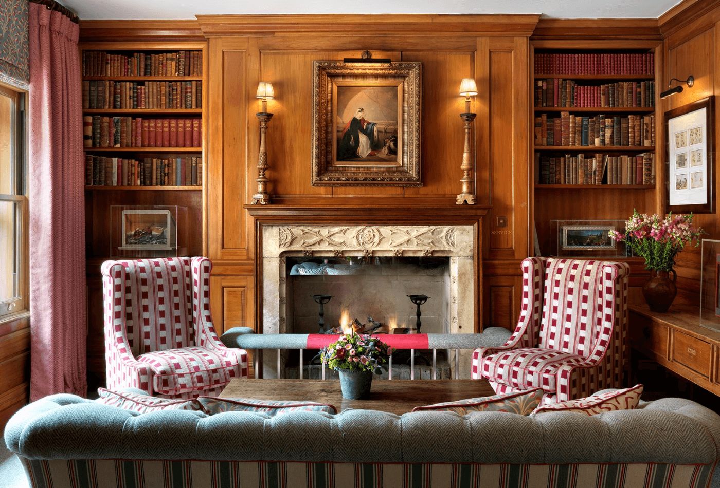 Library room with panelled walls, red patterned chairs and chesterfield sofa